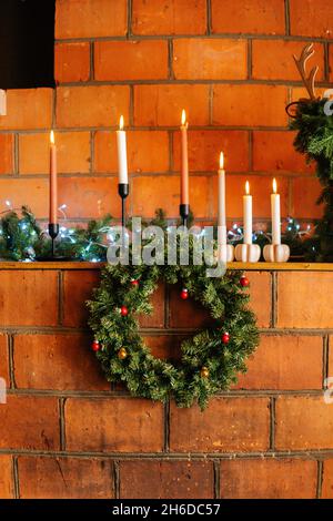 Photo verticale de la belle couronne de Noël accrochée à une cheminée en brique avec bougies allumées dans la maison avec intérieur moderne. Banque D'Images