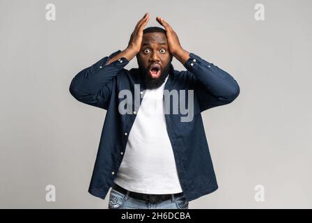 Un gars afro-américain étonné isolé sur gris, choqué homme multiracial tenant la tête et regardant la caméra avec la bouche ouverte, dazed sombre-skinned mâle publicité meilleure affaire, vente.Copier l'espace Banque D'Images