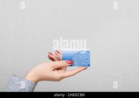 Main féminine tenant une carte de crédit bleue sur un fond de mur Banque D'Images