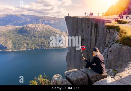 Blonde touriste avec le drapeau de la Norvège regarde le panorama de preikestolen.Attraction touristique.Temps ensoleillé dans les montagnes - Norvège Banque D'Images