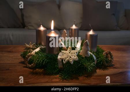 Couronne de l'Avent avec bougies dorées et décoration de Noël naturelle sur une table basse en bois, une flamme brûle pour le premier des quatre dimanches, espace de copie Banque D'Images
