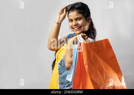 Une belle femme indienne en robe jaune avec des sacs de shopping regardant l'appareil photo sur fond blanc Banque D'Images