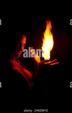 Une femme tient le feu dans la paume de sa main en regardant la caméra Banque D'Images