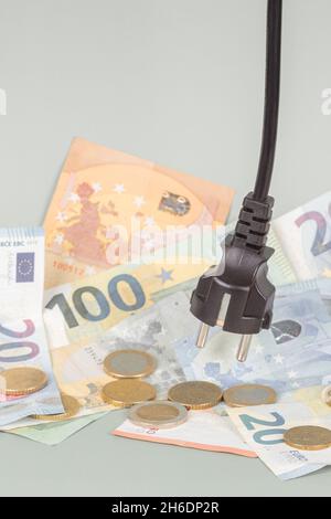 Branchez le cordon d'alimentation sur une pile de pièces et de billets en euros.Efficacité énergétique, consommation d'énergie, coût de l'électricité et concept énergétique coûteux Banque D'Images