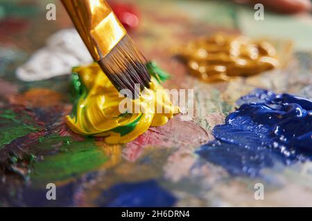 Peintre mélange de peintures jaunes et vertes avec un pinceau Banque D'Images