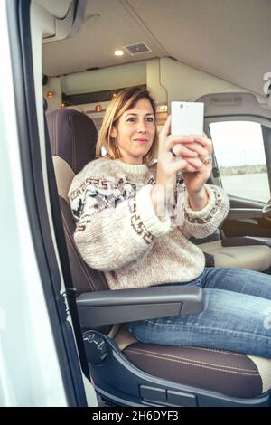 Femme prenant des photos avec un téléphone portable assis dans une camionnette de camping Banque D'Images