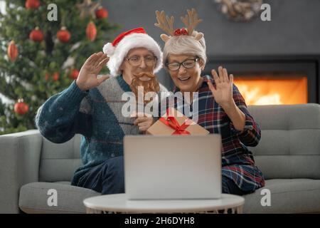 Un couple senior discute avec quelqu'un en utilisant un ordinateur portable dans la salle de séjour décorée pour Noël. Banque D'Images