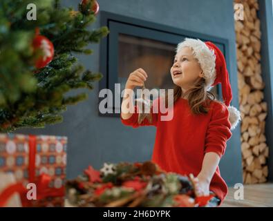 Joyeux Noël et joyeuses fêtes.Mignon petite fille d'enfant est la décoration de l'arbre à l'intérieur.Le matin avant Noël. Banque D'Images