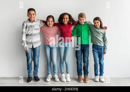 Groupe de jeunes enfants heureux et variés qui s'embrassent sur fond gris Banque D'Images