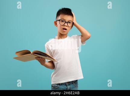 Fatigué de l'étude.Met l'accent sur le livre de maintien et la tête touchante pour petit garçon asiatique Banque D'Images