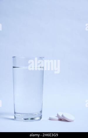 Verre d'eau propre et des pilules sur fond gris Banque D'Images