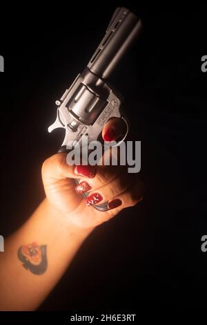 Détective Lady SPY avec vernis à ongles rouge peint tenant pistolet pistolet la nuit Banque D'Images