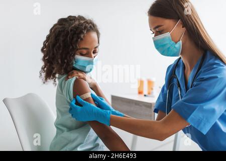 Travailleur médical vaccinant la fille pré-adolescent noire faire la vaccination en clinique Banque D'Images