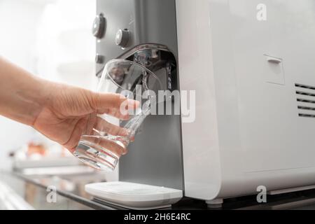 Main rapprochée de la femme remplissant le verre avec l'eau de la glacière , machine à eau potable Banque D'Images