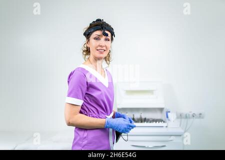 Portrait d'une femme médecin confiante.Femme médecin ORL dans des vêtements médicaux pourpres posant au bureau de la clinique sur sa tête avec un instrument de sedecin Banque D'Images
