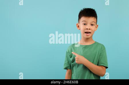 Un petit garçon asiatique excités pointant de côté à l'espace de copie sur fond bleu Banque D'Images