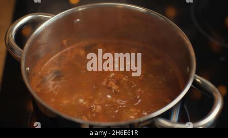 Gros plan de la délicieuse soupe russe traditionnelle solyanka bouillant dans un pot sur la cuisinière.Soupe russe de solyanka avec viande, saucisses et olives Banque D'Images