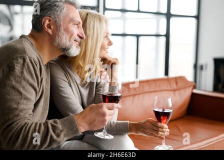Vue latérale sur un couple romantique d'âge moyen qui tient des verres avec du vin, les conjoints adultes passent la soirée ensemble, ont une date, célébrant les vacances Banque D'Images