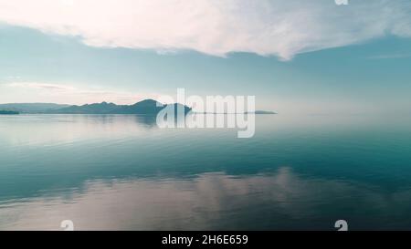 L'eau en miroir reflète le ciel bleu avec l'horizon de la montagne.Prise de vue.Paysage pittoresque avec reflet du ciel bleu dans la surface tranquille de la mer.Fusion de la mer a Banque D'Images