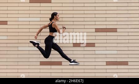 Style de vie actif.Athletic Young Lady in Sportswear running over Brick Urban Wall Banque D'Images