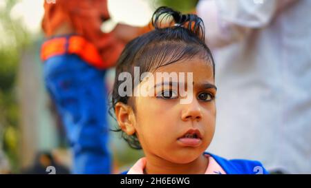 Une petite fille indienne innocente portant un chandail bleu et regardant l'appareil photo.Cheveux bouclés petite fille gros plan. Banque D'Images