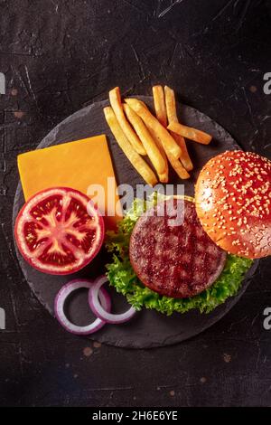 Ingrédients de hamburger de bœuf, tiré d'en haut sur un fond sombre.Hamburger bœuf patty steak avec pommes de terre et légumes Banque D'Images