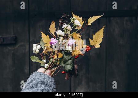 Photo stylisée.Composition féminine d'automne.Gros plan des mains de la femme tenant des fleurs et des feuilles d'automne colorées bouquet.Cyclamen rose et rouge Banque D'Images