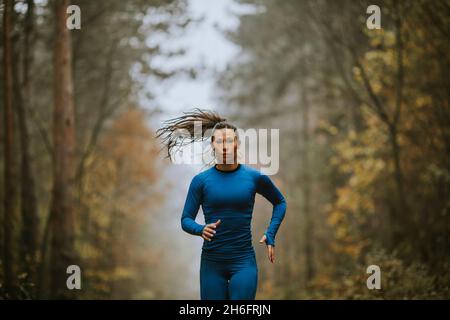 Jeune femme en costume bleu de course vers la caméra sur le sentier forestier à l'automne Banque D'Images