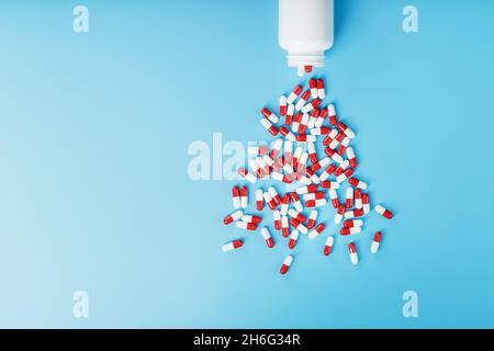 Une dispersion de comprimés rouges et blancs capsules d'un pot blanc sur fond bleu.Produits pharmaceutiques, médicaments, vitamines Banque D'Images