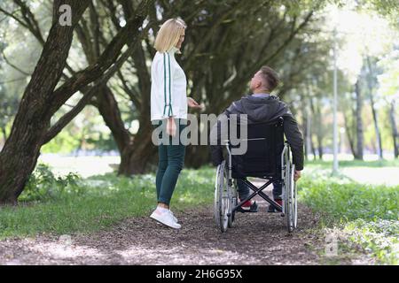 Une jeune femme souriante marche dans le parc avec un homme en fauteuil roulant Banque D'Images