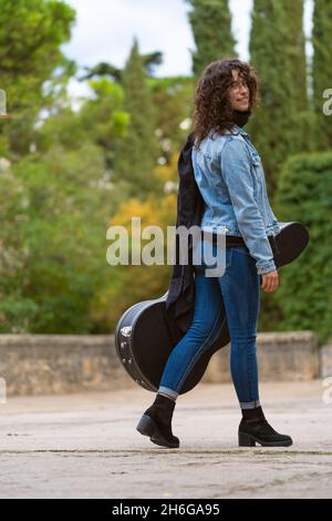 Jeune femme marchant avec sa guitare dans le parc et souriant Banque D'Images