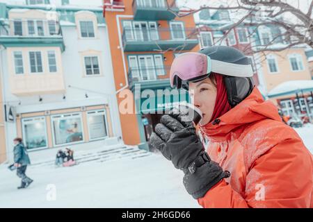 Vacances de ski - femme skieuse buvant du café chaud ou du chocolat sur le ski vacances d'hiver en plein air dans la station de ski.Femme portant des gants et des lunettes de ski Banque D'Images
