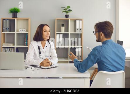 Médecin d'âge moyen assis à son bureau et ayant une conversation avec sa patiente Banque D'Images