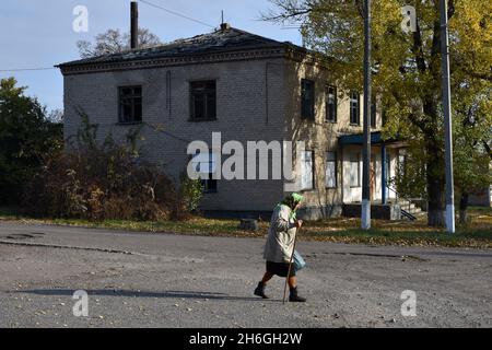 Verkhnocketske, Donetsk, Ukraine.16 octobre 2021.Une dame âgée est vue passer par un bâtiment endommagé dans le centre du village de Verkhnocketske.Verkhnocketske est un village ukrainien de type urbain situé sur la ligne de front même dans le district de Yasynuvata dans l'oblast de Donetsk dans l'est de l'Ukraine.Au cours de la guerre du Donbass, qui a débuté à la mi-avril 2014, la ligne de séparation entre les parties belligérantes a été située à proximité de la colonie.Le village était une zone grise jusqu'à la fin de 2017.Aujourd'hui, Verkhnocketske est un territoire de l'Ukraine.Le conflit a entraîné à la fois des civils et Banque D'Images