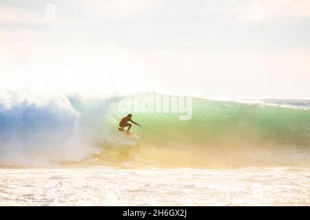 Surfeur qui sort de la vague, soleil en arrière-plan, lumière chaude Banque D'Images