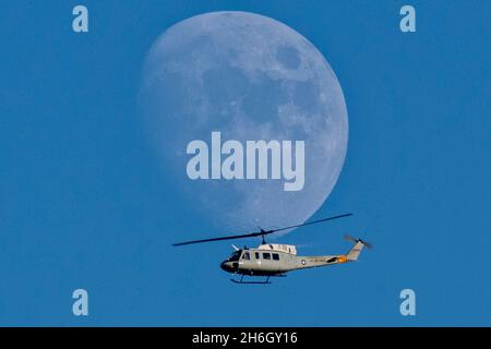 Yokota, Japon.11 mars 2021.Une lune de phase Gibbous cirée s'est illuminée à la lumière du jour alors qu'un hélicoptère Iroquois UH-1N de la US Air Force, affecté au 459e Escadron de transport aérien, passe devant une mission d'entraînement au-dessus de la base aérienne de Yokota le 15 novembre 2021 à Yokota, au Japon.Crédit : Osakabe Yasuo/États-UnisAir Force/Alamy Live News Banque D'Images