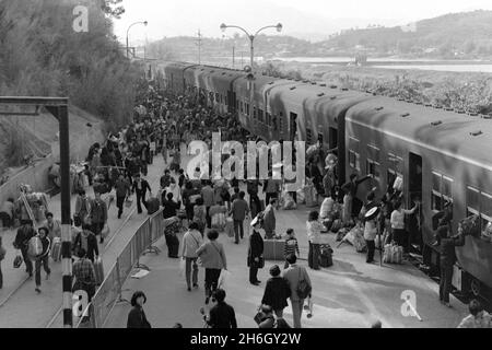 Gare de Lo Wu, Hong Kong. Vue depuis le toit de la gare - vue au sud - des passagers sortant d'un train, en direction de la Chine continentale à l'année lunaire du nouvel an, 1981. Beaucoup portent des cadeaux pour des parents, en utilisant des yokes de bambou pour équilibrer leurs colis. Les trains diesel ont été progressivement éliminés lorsque le chemin de fer Kowloon-Canton (section HK) a été électrifié au début de 1980s Banque D'Images