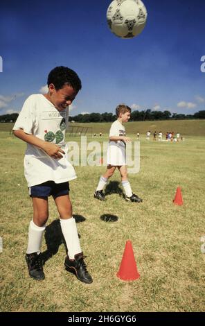 Austin Texas USA, vers 1989: Un garçon d'âge élémentaire pratique un ballon de football avec sa tête dans un camp de football d'été enfants dans un parc local.©Bob Daemmrich Banque D'Images