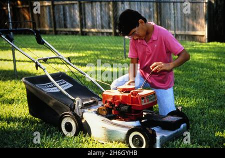 Austin Texas USA, vers 1989: Adolescent garçon, 12 ans, travaillant sur une tondeuse à gazon pour terminer un travail d'été fauchant des pelouses, ©Bob Daemmrich Banque D'Images