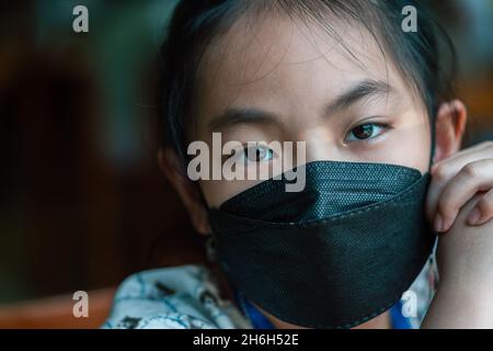 Gros plan de l'enfant asiatique fille à 8 ans portant la marque médicale noire, les yeux émotionnels regardent la caméra. Banque D'Images