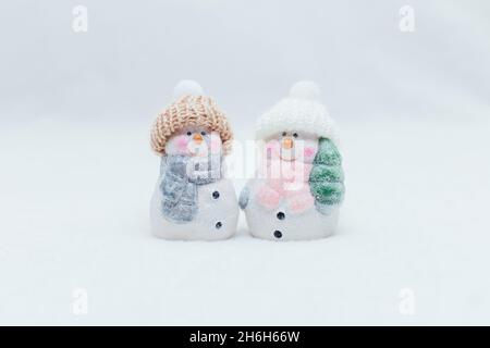 Figurines décoratives sur le thème de Noël.Deux statuettes d'un bonhomme de neige dans un chapeau tricoté sur fond blanc.Décoration festive, lumières bokeh chaleureuses Banque D'Images