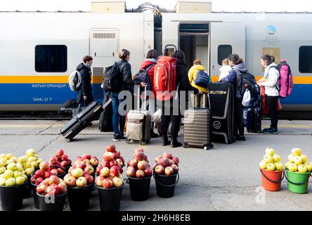 Passagers à bord d'un train à un arrêt de train.Les seaux avec des pommes fraîches d'automne sont mis sur le sol pour la vente par des vendeurs locaux.Almaty, Kazakhstan Banque D'Images