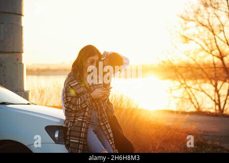 Le voyageur de couple se tient en voiture au coucher du soleil dans la campagne.Elle utilise la carte des applications mobiles dans son smartphone pour trouver le chemin.Les touristes qui vérifient la position dans la carte du smartphone.Mise au point douce Banque D'Images