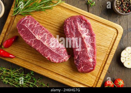 Steak de bœuf frais composé de deux lames sur une planche à bois, avec condiments et herbes Banque D'Images
