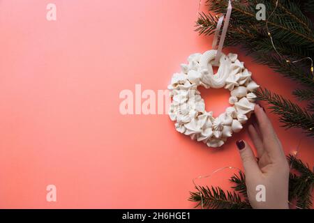 Couronne de Noël à la meringue sur la branche de sapin sur le fond de couleur corail vivant.Concept de carte.Vue de dessus.Pose à plat Banque D'Images