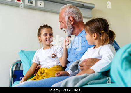 Heureux petits-enfants en visite chez le grand-père à l'hôpital. Concept de soutien, de famille et de soins de santé. Banque D'Images