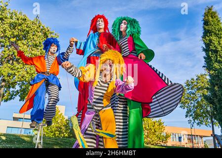 Un petit angle de clowns gaies, hommes et femmes, vêtus de costumes et de perruques colorés, souriant tout en effectuant un spectacle sur pilotis et monocycle pendant le festival dans le parc de la ville Banque D'Images