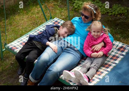 Grand-mère et ses deux petits-enfants s'amusent sur une balançoire, leur petit-fils et leur petite-fille aiment leur granny.Des hors-d'eux relaxants dans la campagne du grand-mère de Hou Banque D'Images