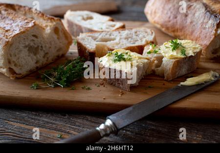 Baguette française coupée en tranches de beurre sur une planche à découper rustique en bois avec couteau Banque D'Images