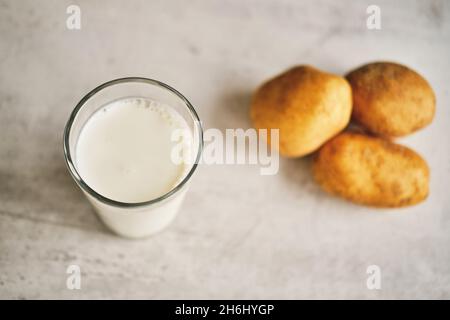 Un verre transparent avec du lait de pomme de terre sur la table à côté des tubercules de pomme de terre. Banque D'Images